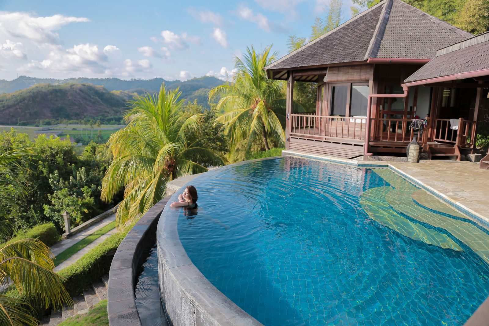 A woman relaxes in an infinity pool overlooking tropical scenery at a Bali villa.